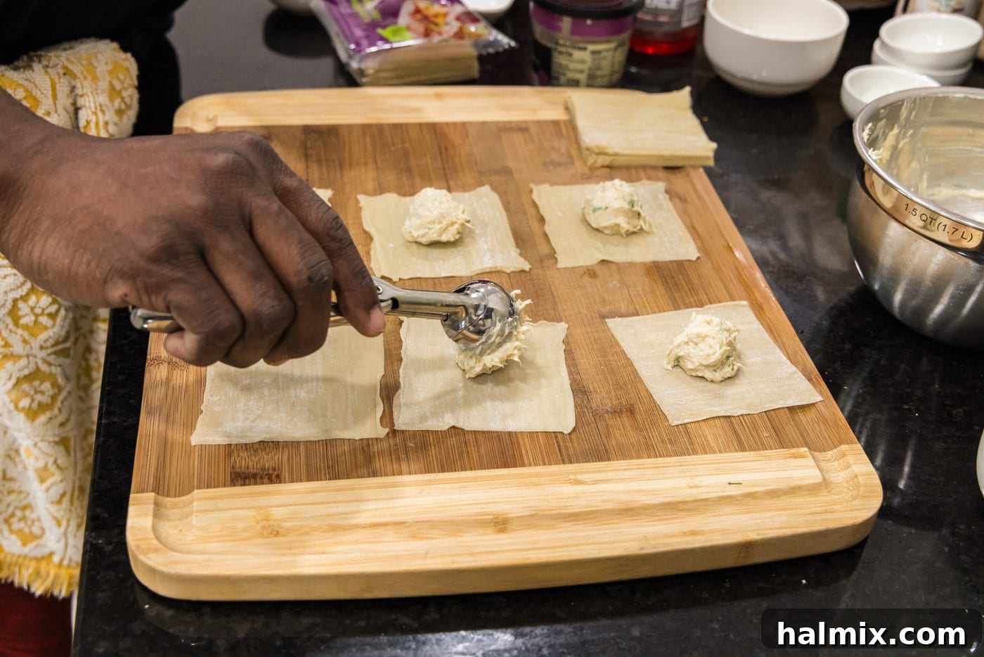 Scooping crab filling into the center of wonton wrappers on a flat surface.