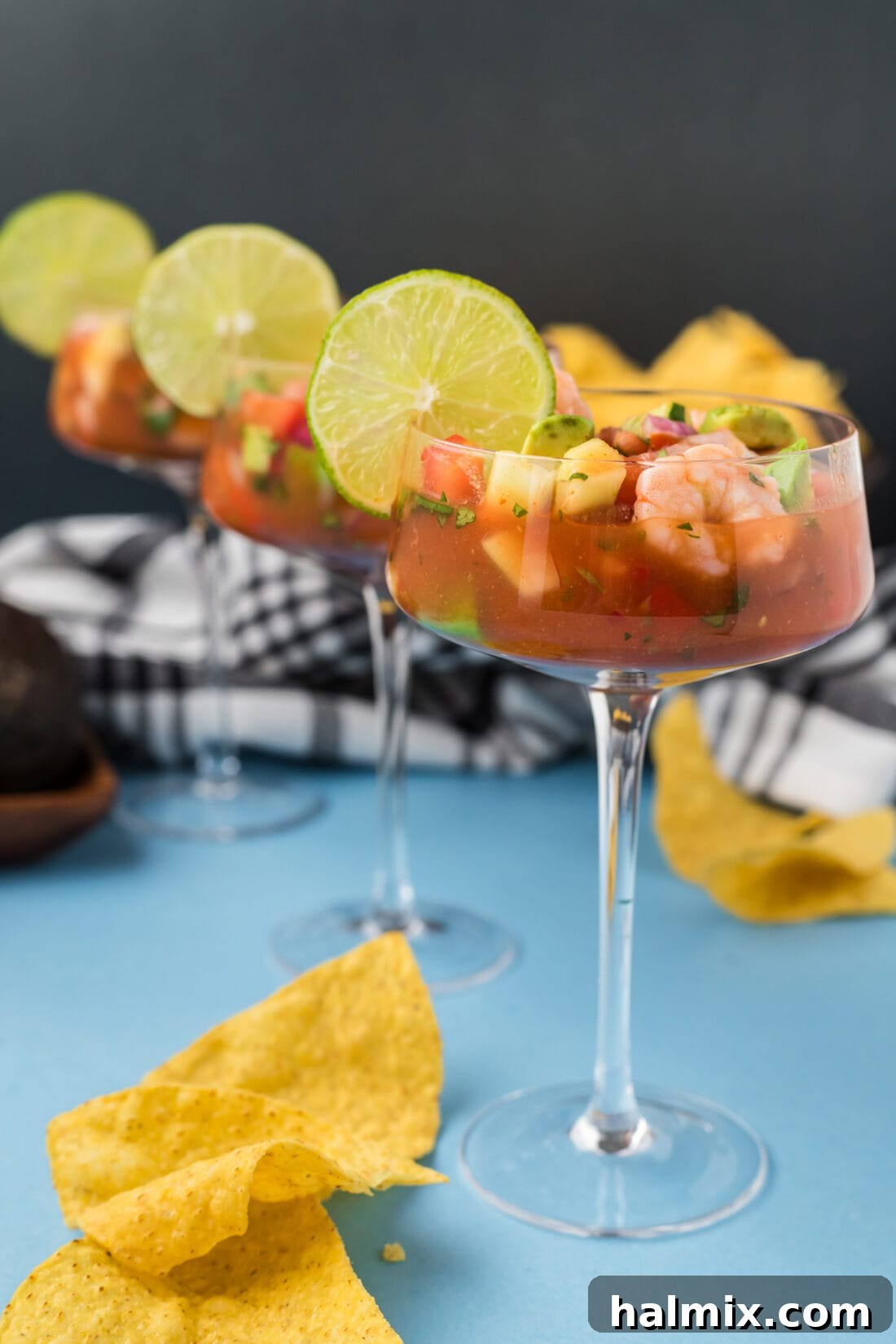 Three elegant servings of Mexican Shrimp Cocktail in glasses, garnished with lime wedges and cilantro, lined up on a wooden table