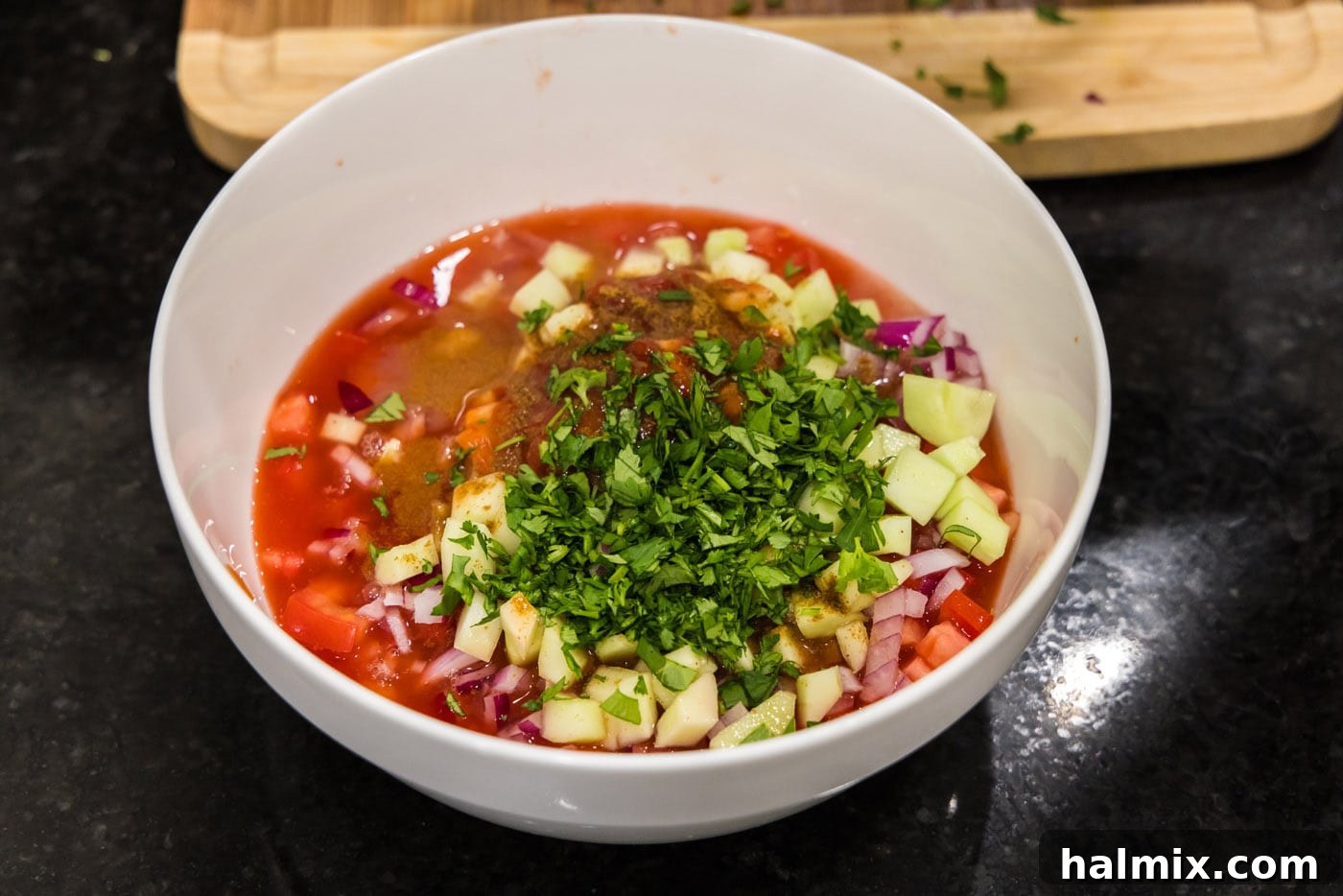 A mixing bowl filled with the complete broth base, including Clamato juice, ketchup, hot sauce, citrus juices, cumin, and chopped cilantro, mixed with the vegetables