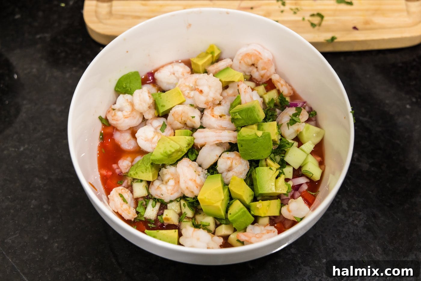 Chopped avocado and cooked, chilled shrimp being added to the large mixing bowl with the Mexican shrimp cocktail ingredients