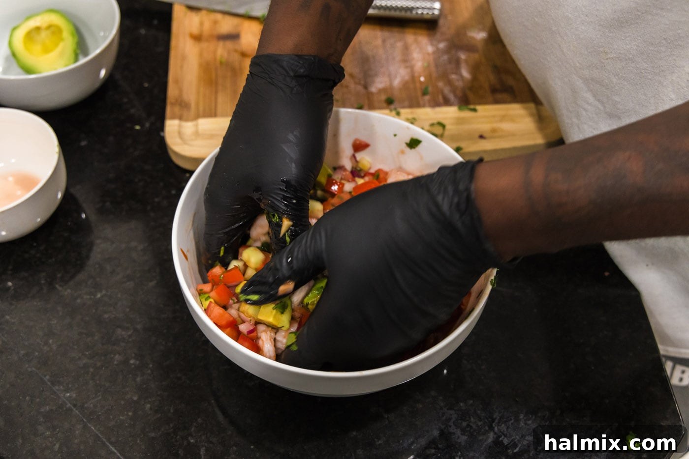Hands wearing gloves gently tossing the Mexican shrimp cocktail ingredients in a large bowl to ensure everything is well combined