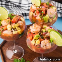 Three Mexican Shrimp Cocktails in individual glasses presented on a wooden serving tray, garnished with lime wedges