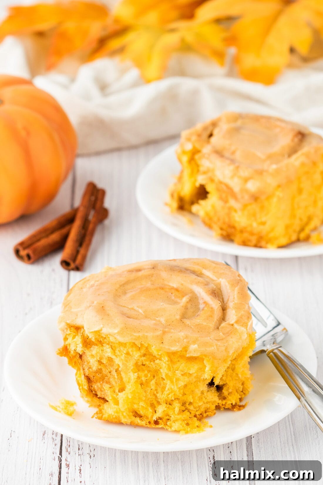 Two Pumpkin Cinnamon Rolls on plates, garnished with a light dusting of cinnamon