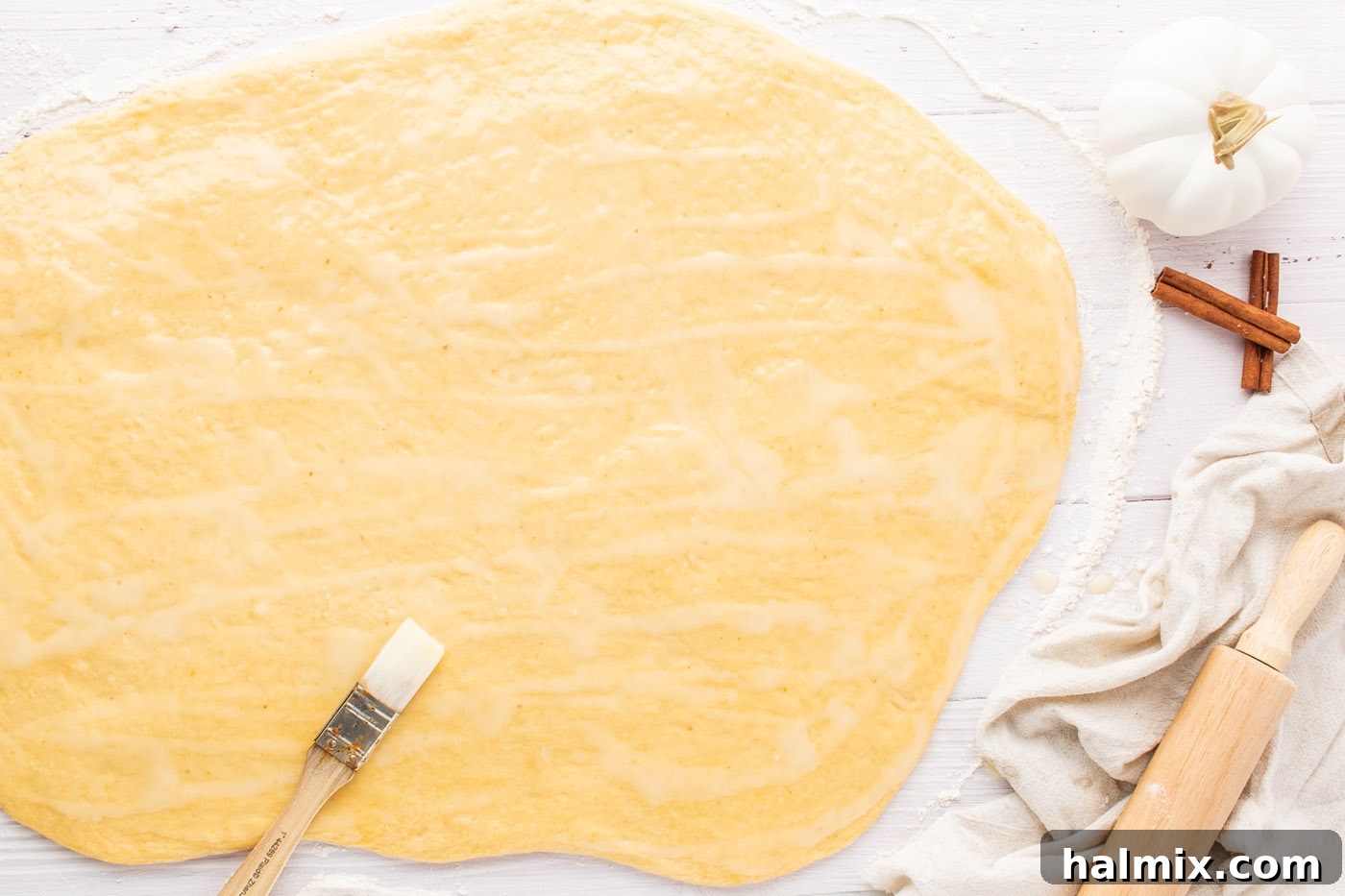 Softened butter being spread meticulously over the surface of rolled-out cinnamon roll dough