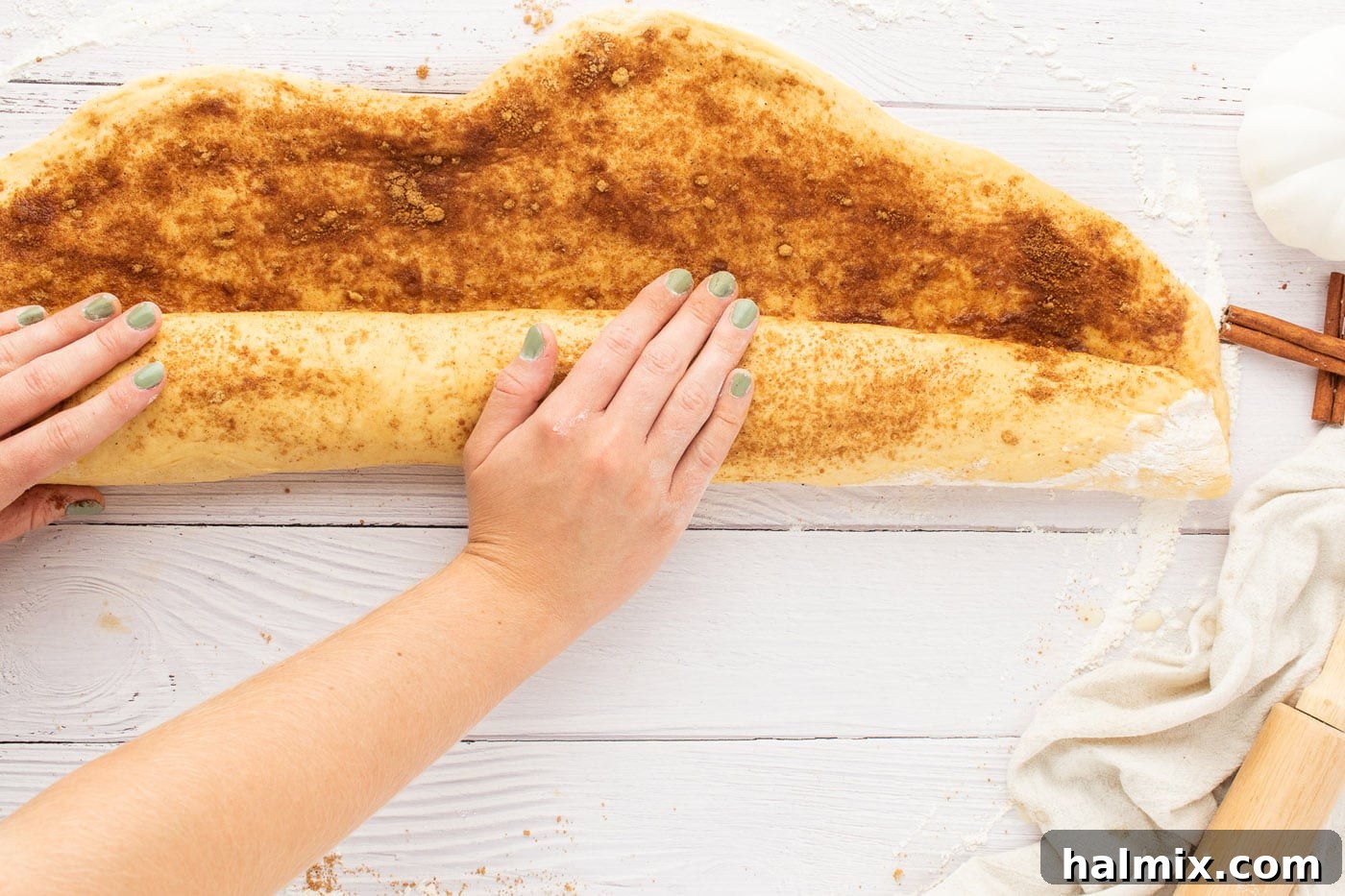 Cinnamon roll dough being carefully rolled into a log shape after filling