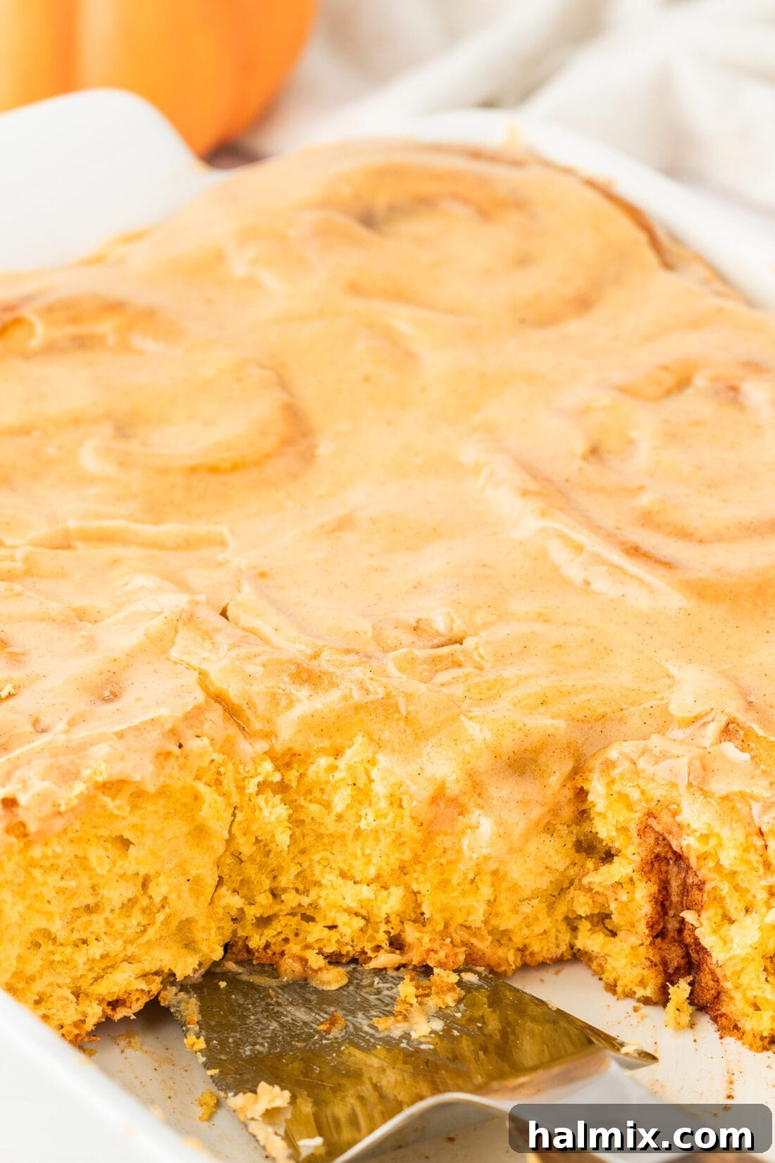 A close-up photograph of an entire pan of freshly baked and frosted Pumpkin Cinnamon Rolls, showcasing their soft texture and generous frosting