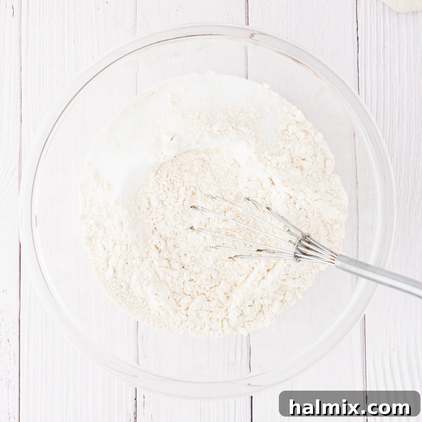 Large mixing bowl containing flour, sugar, and salt, with a whisk resting inside