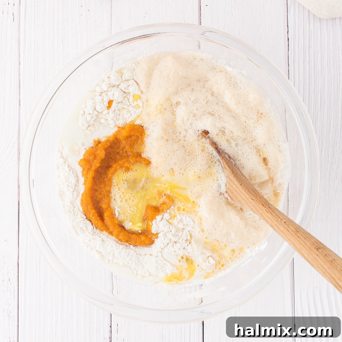 Various wet ingredients including softened butter, eggs, vanilla, pumpkin puree, warm milk, and yeast mixture being added to a mixing bowl