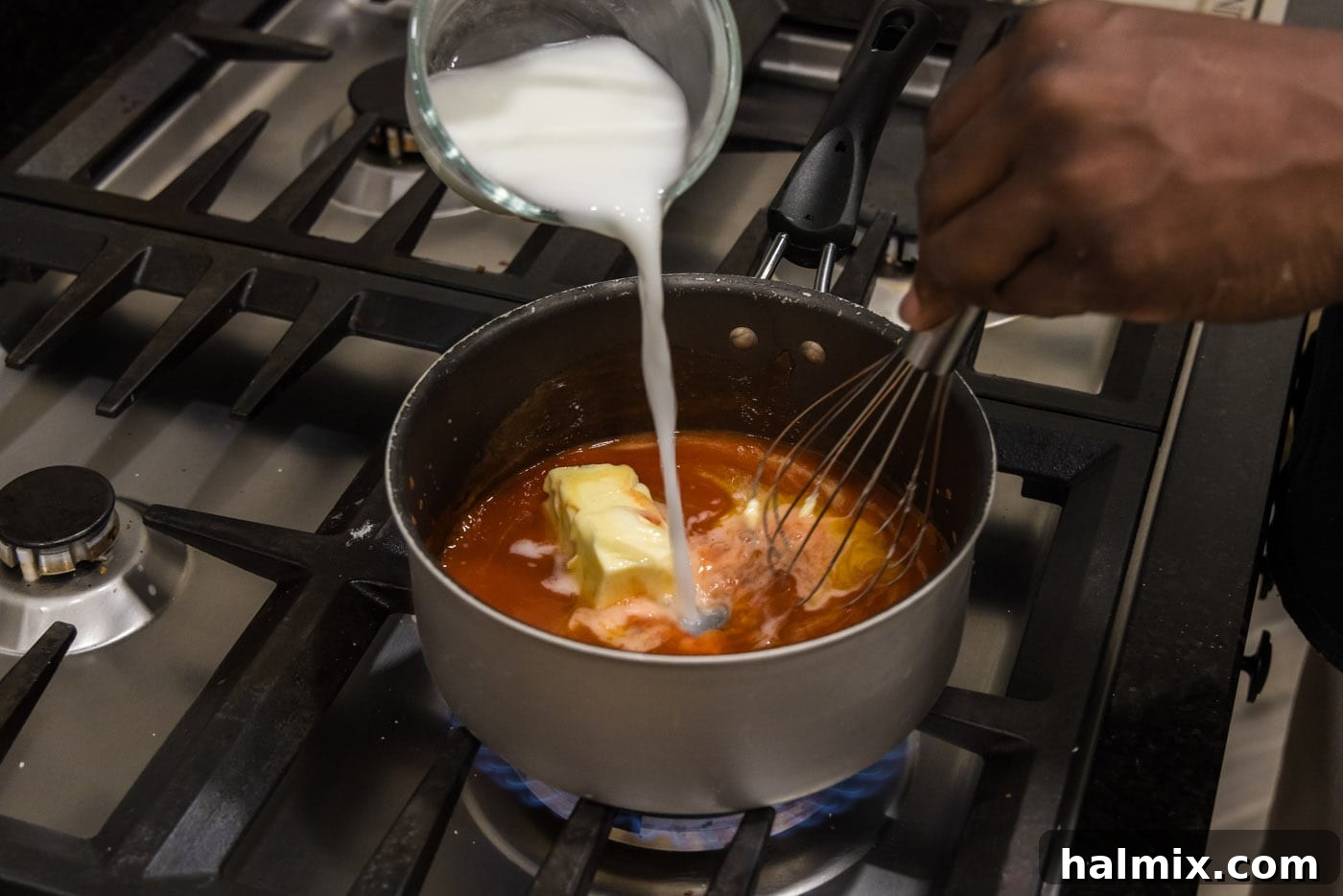 Whisking a cornstarch slurry into the buffalo sauce mixture in a saucepan.