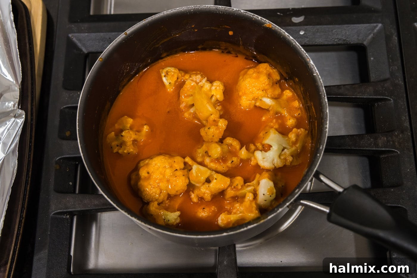 Tossing baked cauliflower florets in buffalo sauce to coat them evenly.