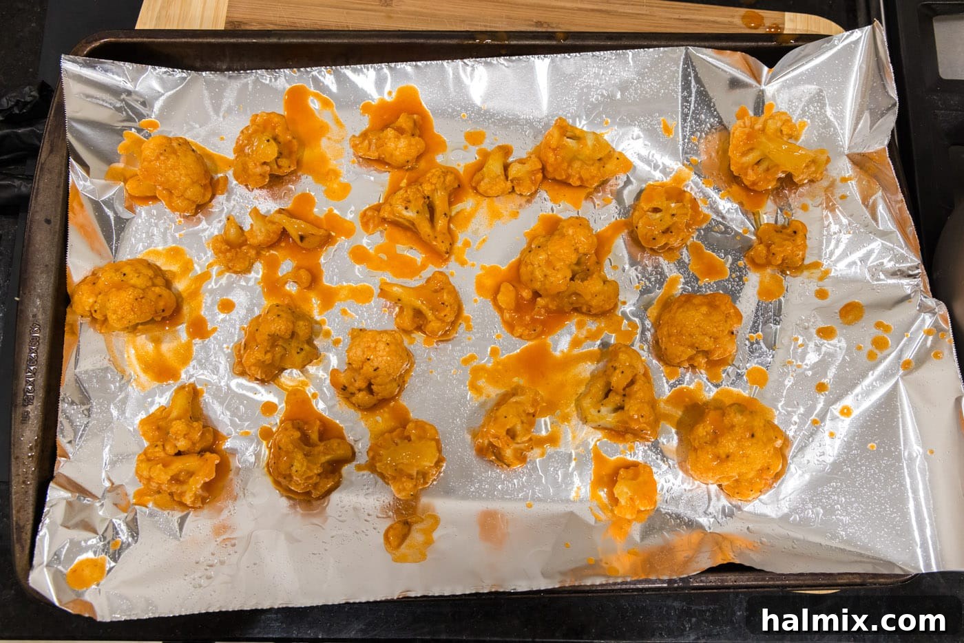 Buffalo cauliflower wings baked and ready on a baking sheet, glistening with sauce.