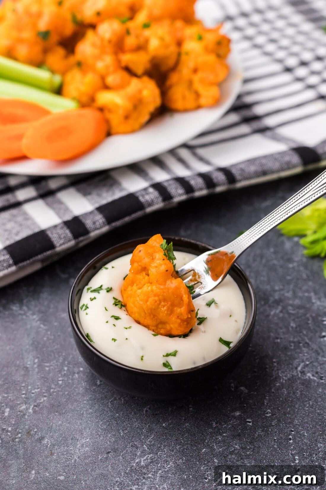 A buffalo cauliflower wing being dipped into a bowl of creamy ranch dressing.