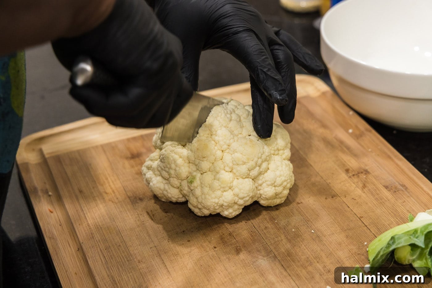 Continuing to slice a head of cauliflower, separating florets.