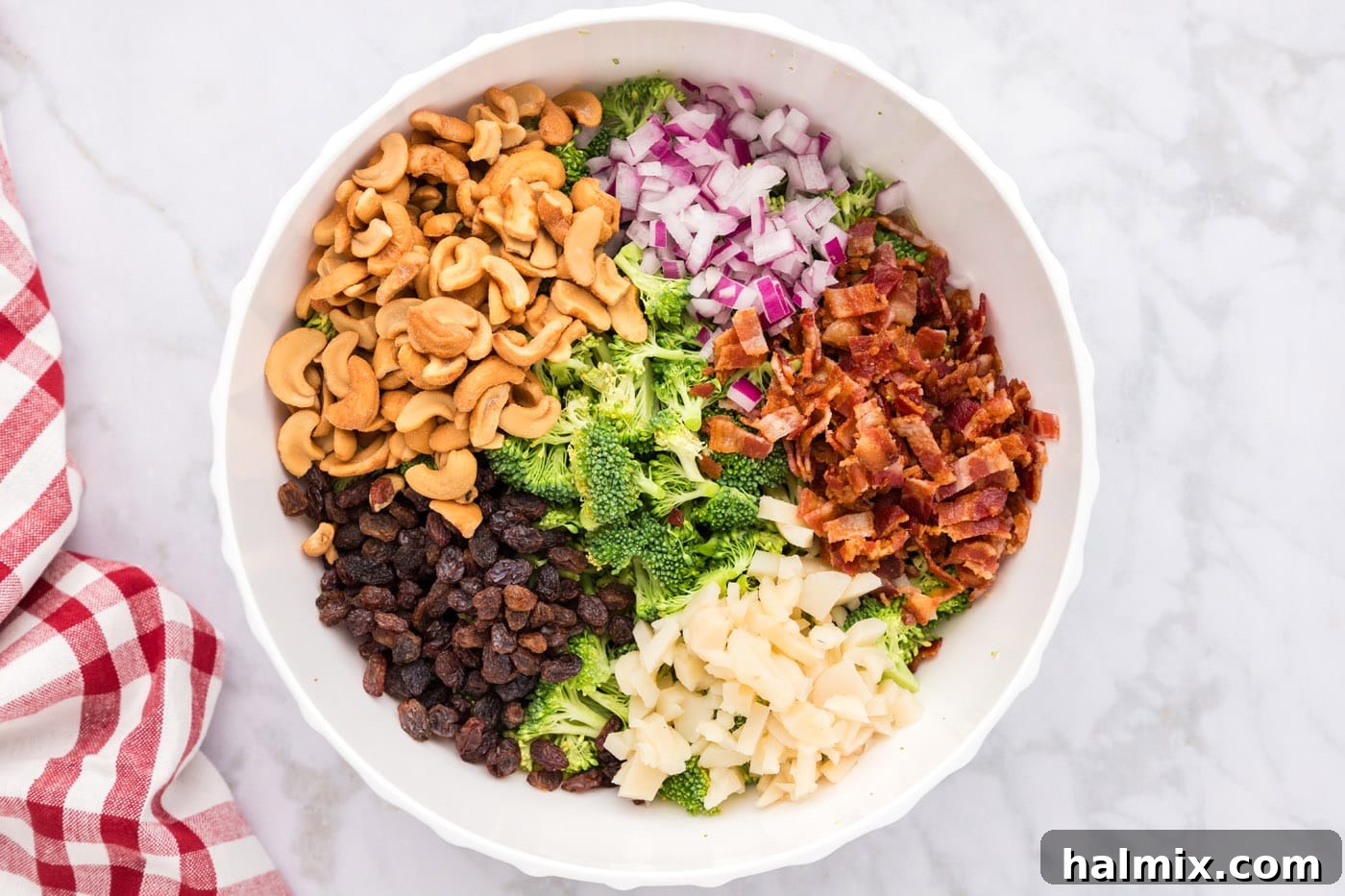 bacon, raisins, cashews, water chestnuts, and onion with broccoli in a bowl
