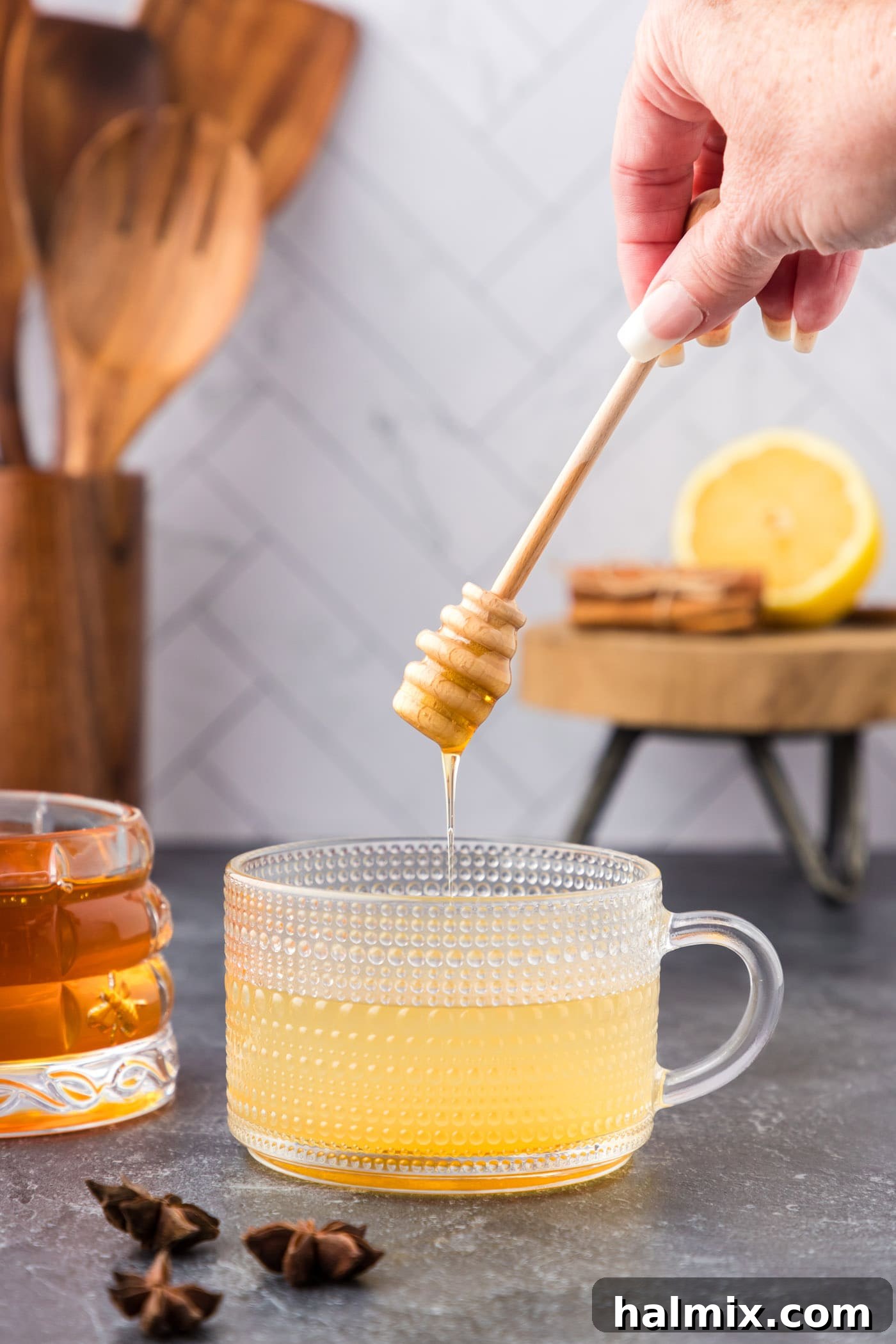 adding honey to glass with whiskey, water, and lemon juice