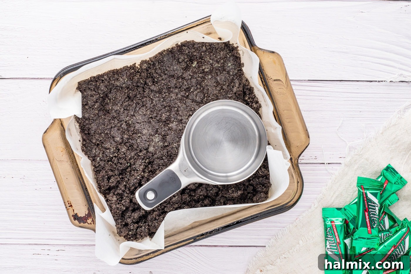 Pressing Oreo crumbs into the bottom of a baking pan to form the crust.