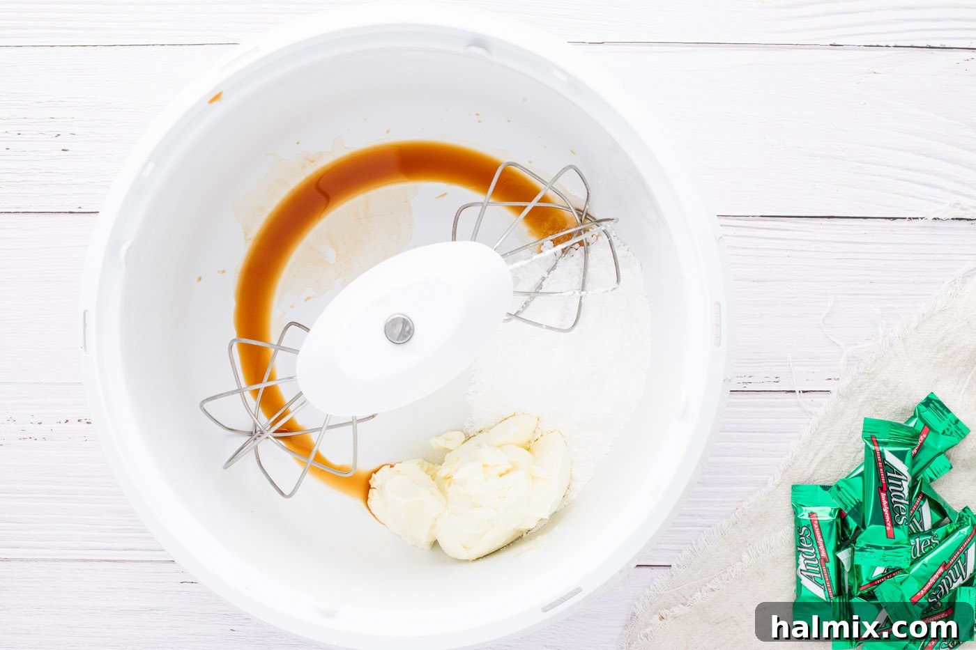 Cream cheese, vanilla, and confectioners' sugar being beaten in a mixer.
