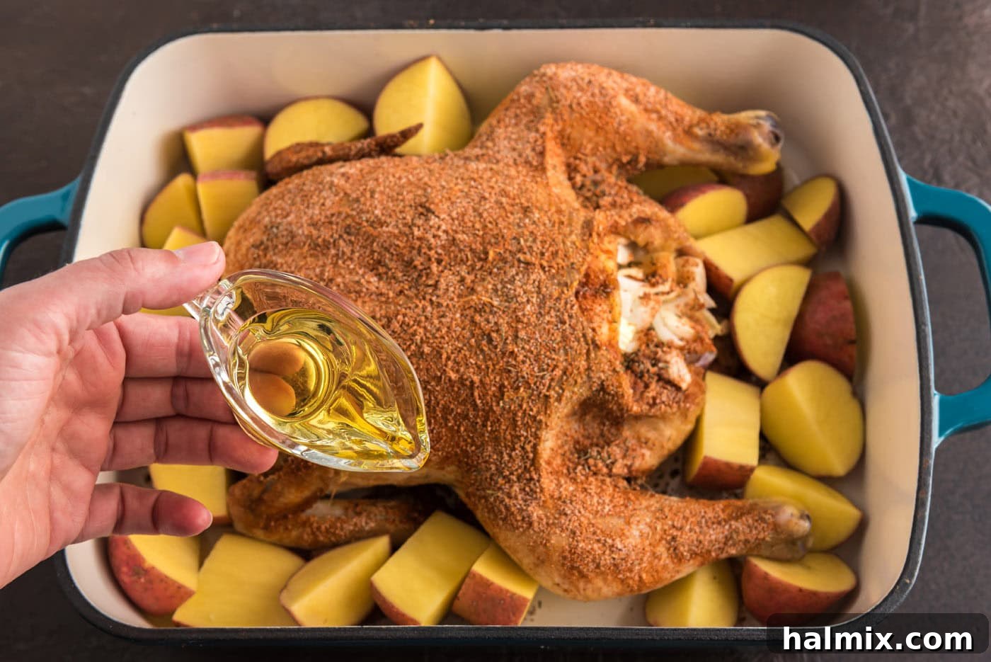 Irresistibly Sticky Slow Roasted Chicken 7 pouring olive oil into pan with whole chicken and red potatoes