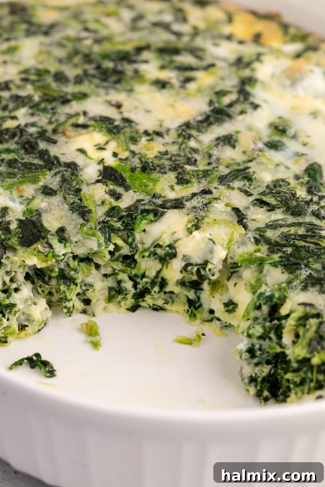 Close up photo of Spinach Souffle with a piece removed, highlighting its creamy, cheesy interior and golden crust.