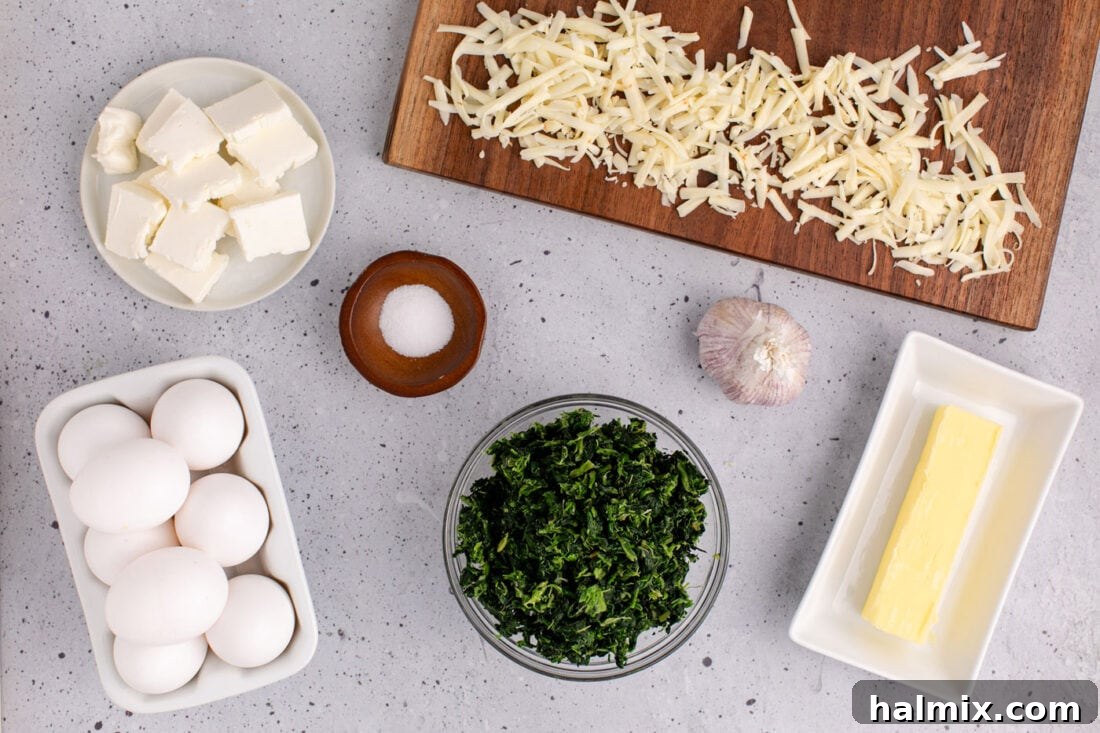 Various ingredients for Spinach Souffle laid out on a wooden cutting board: spinach, eggs, cream cheese, pepper jack cheese, garlic, butter, and salt.