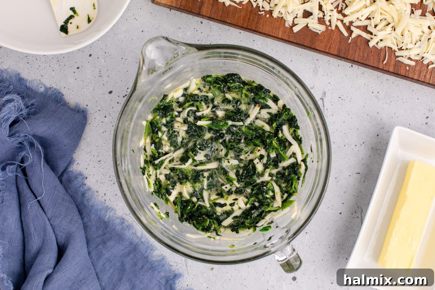 All spinach souffle ingredients thoroughly mixed in a large bowl, showcasing the vibrant green of the spinach and the creamy cheese.