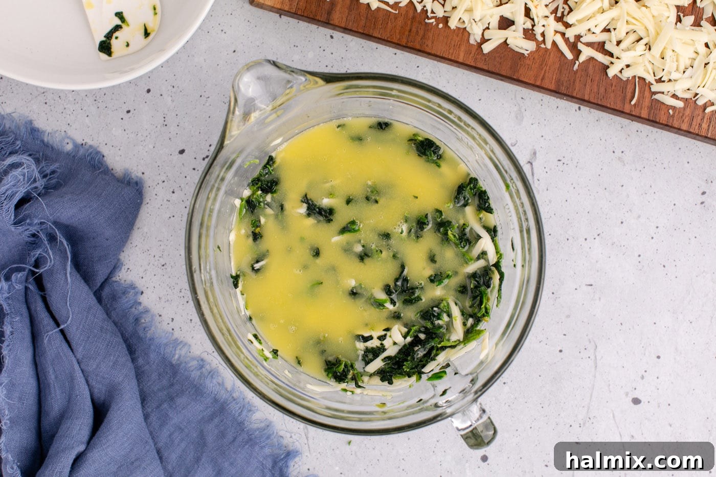Melted butter being poured over the spinach souffle mixture in a bowl, creating a glossy layer.