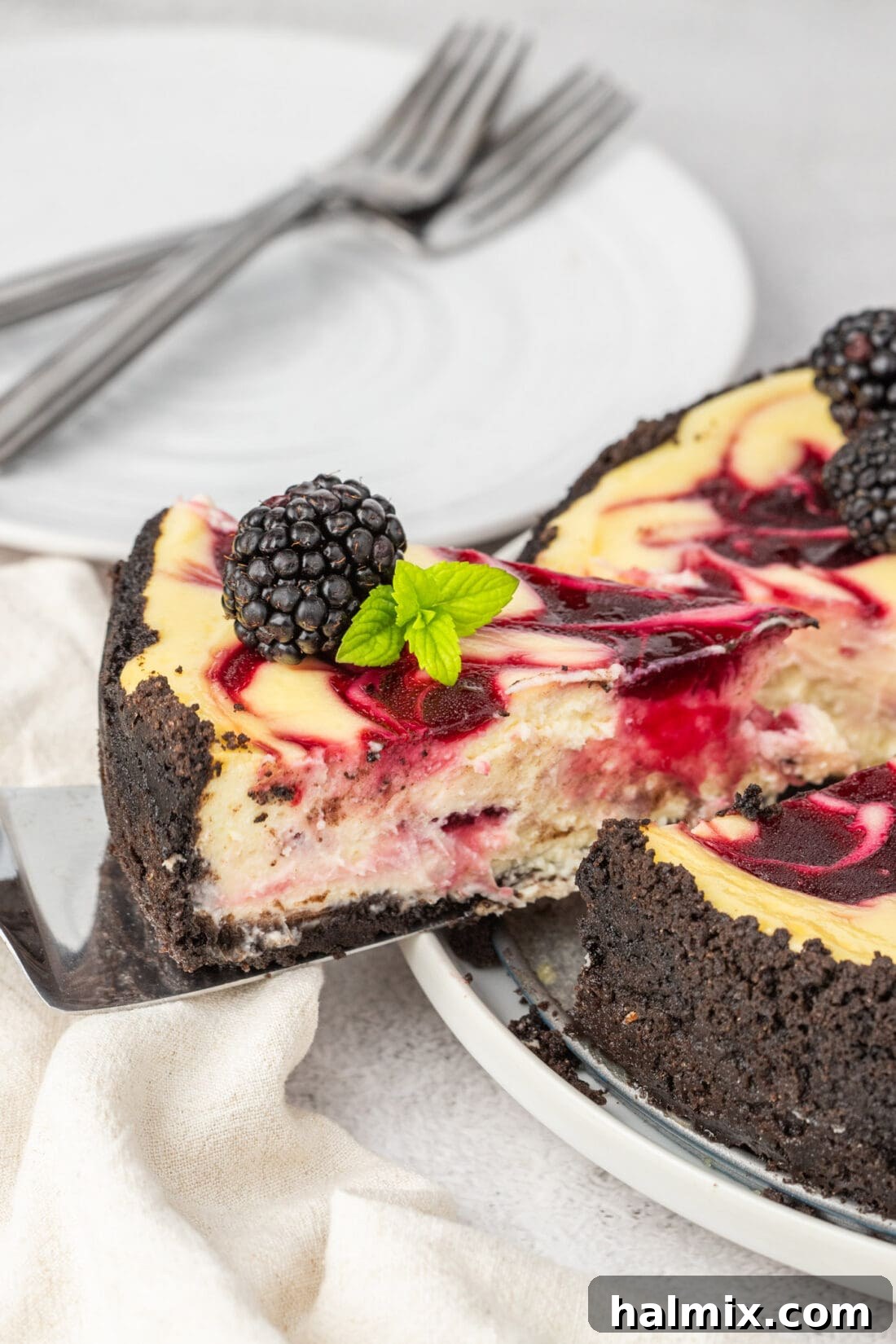 Blackberry Ripple Cheesecake 5 A slice of Blackberry Swirl Cheesecake being carefully lifted from the whole cheesecake, showcasing its elegant swirl pattern.