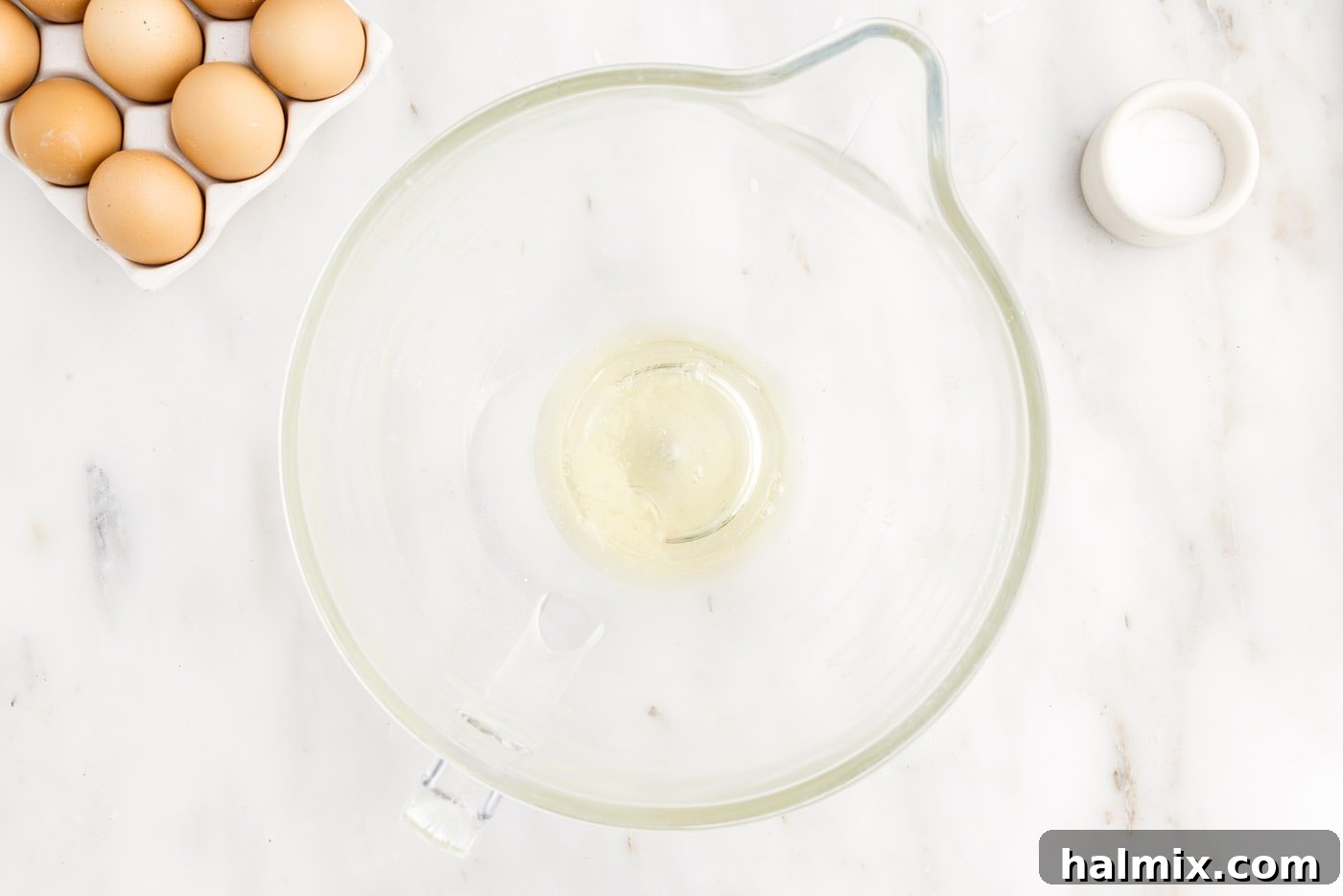 Egg whites and salt beginning to be whisked in a stand mixer bowl, still in liquid form.