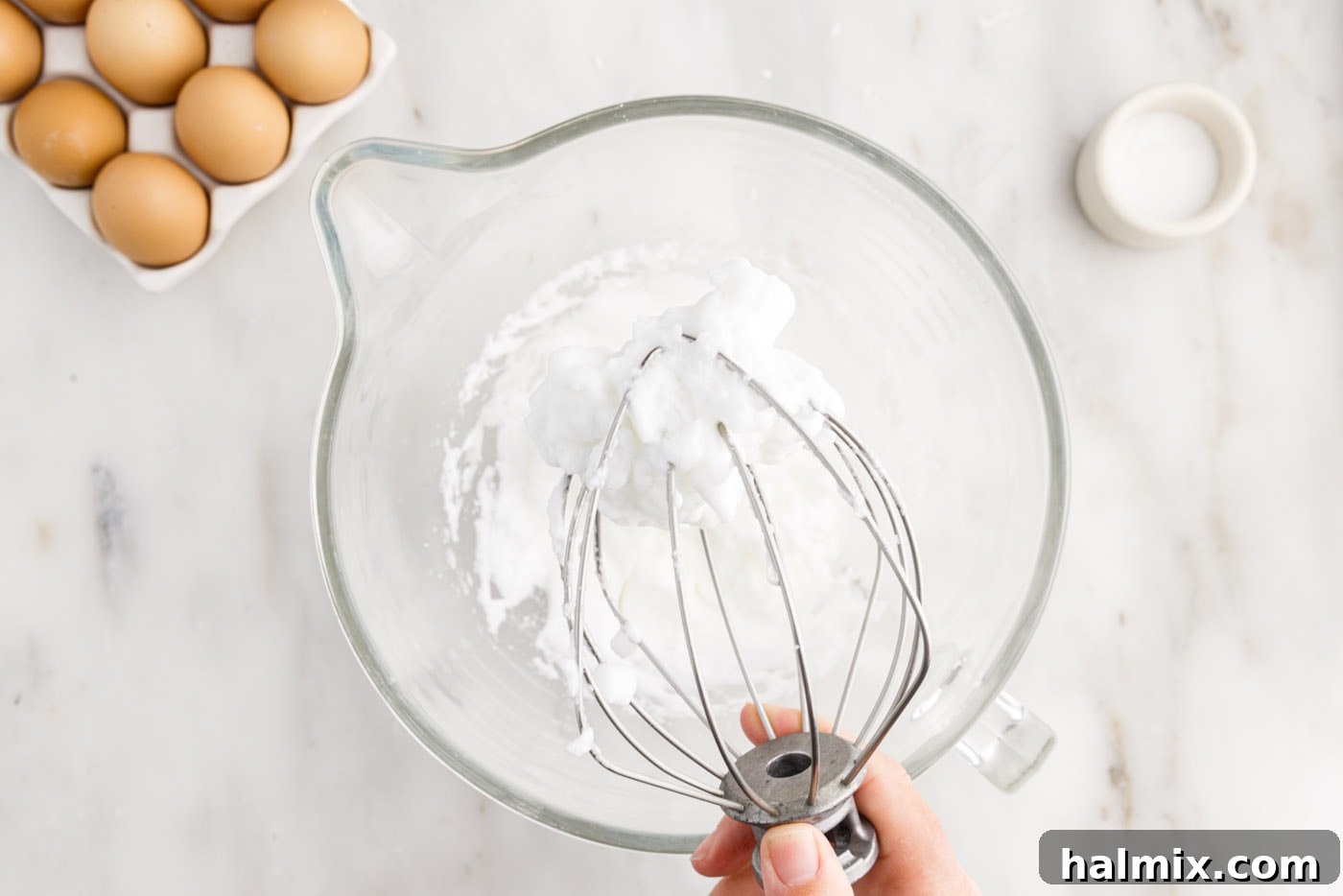 Fully whipped egg whites displaying stiff peaks in a stand mixer bowl, indicating they are ready for the next step.