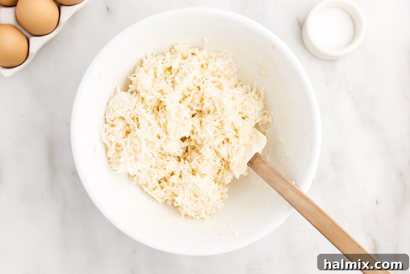 Shredded coconut, sweetened condensed milk, and vanilla mixture fully combined in a bowl, forming a cohesive and sticky base for macaroons.