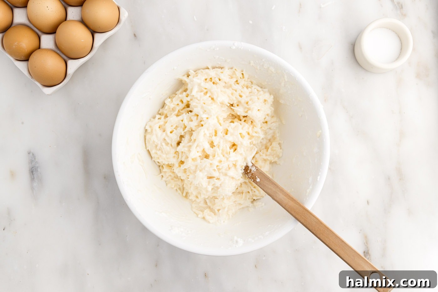 The combined coconut macaroon mixture in a bowl with a rubber spatula, showing the full incorporation of egg whites.