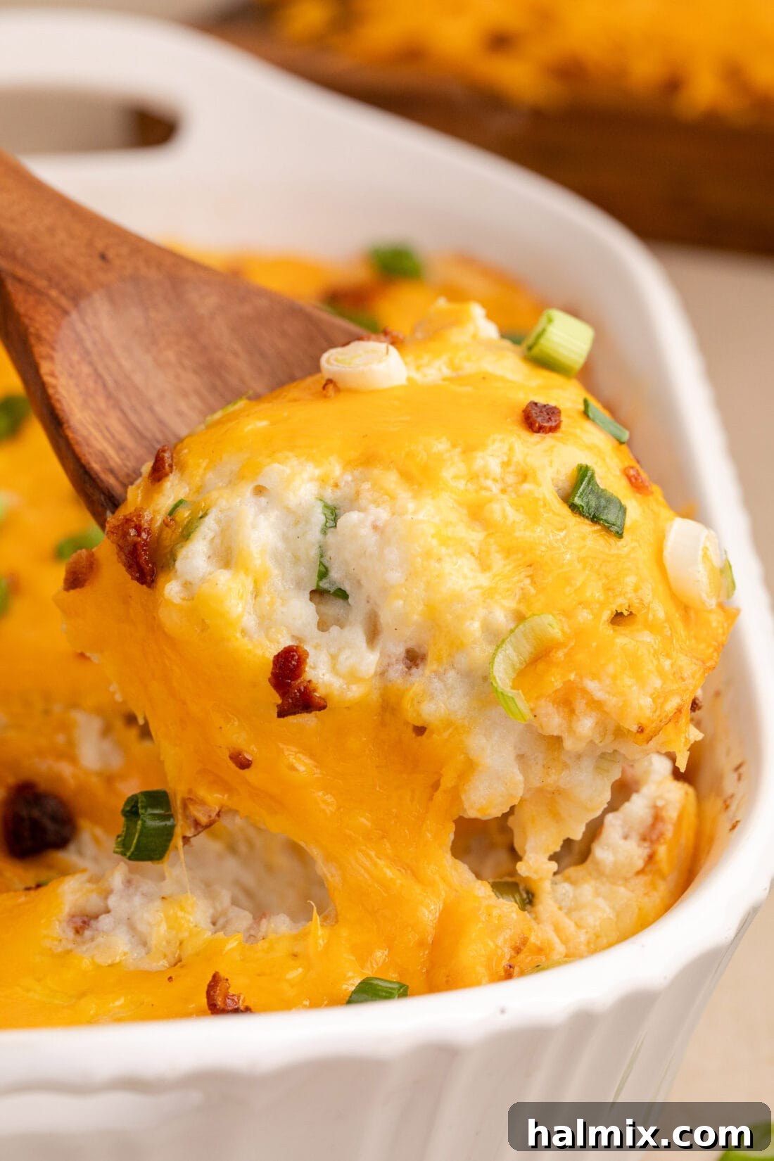 Decadent Twice Baked Potato Casserole 2 A spoonful of creamy Twice Baked Potato Casserole being lifted from the baking dish, revealing layers of cheese and bacon.