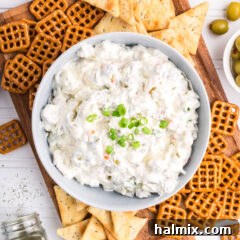 Bowl of Dirty Martini Dip on a board with pretzels and crackers around it