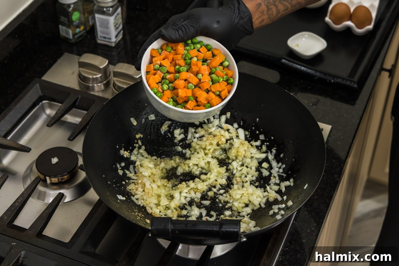 adding frozen peas and carrots to a wok with onion and garlic