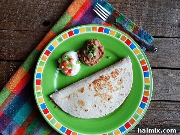 Delicious beef and bean quesadilla served with sour cream and refried beans on a vibrant green plate.