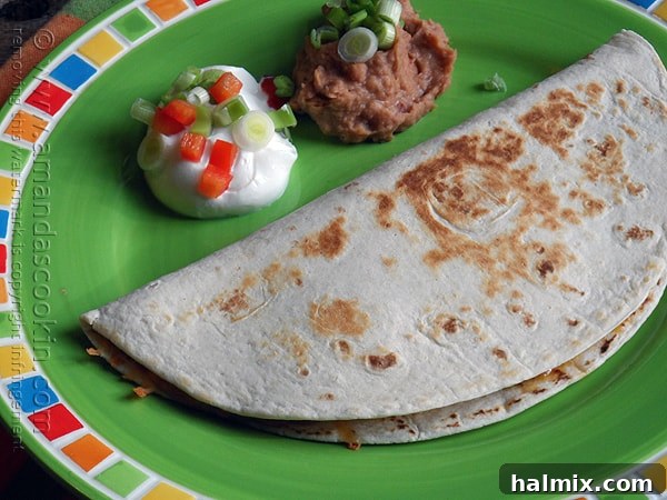 Overhead view of a freshly made beef and bean quesadilla on a green plate, accompanied by dollops of sour cream and a side of refried beans.