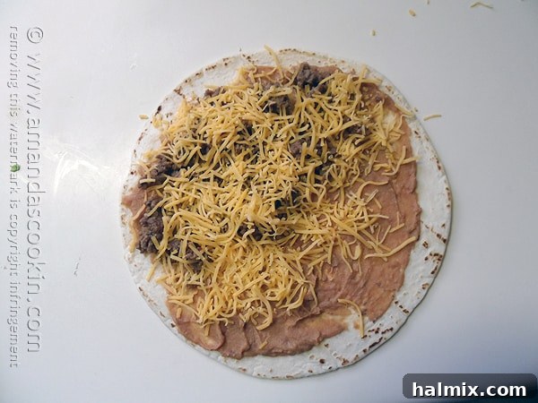 A close-up of a tortilla layered with refried beans, ground beef, and a generous sprinkle of shredded cheese, ready for folding.