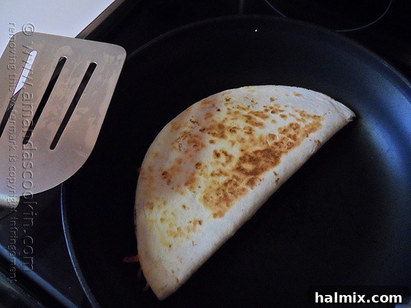 A perfectly folded beef and bean quesadilla sizzling gently in a hot skillet, edges beginning to crisp.