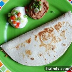 A delicious beef and bean quesadilla on a green plate, with sour cream and refried beans on the side.