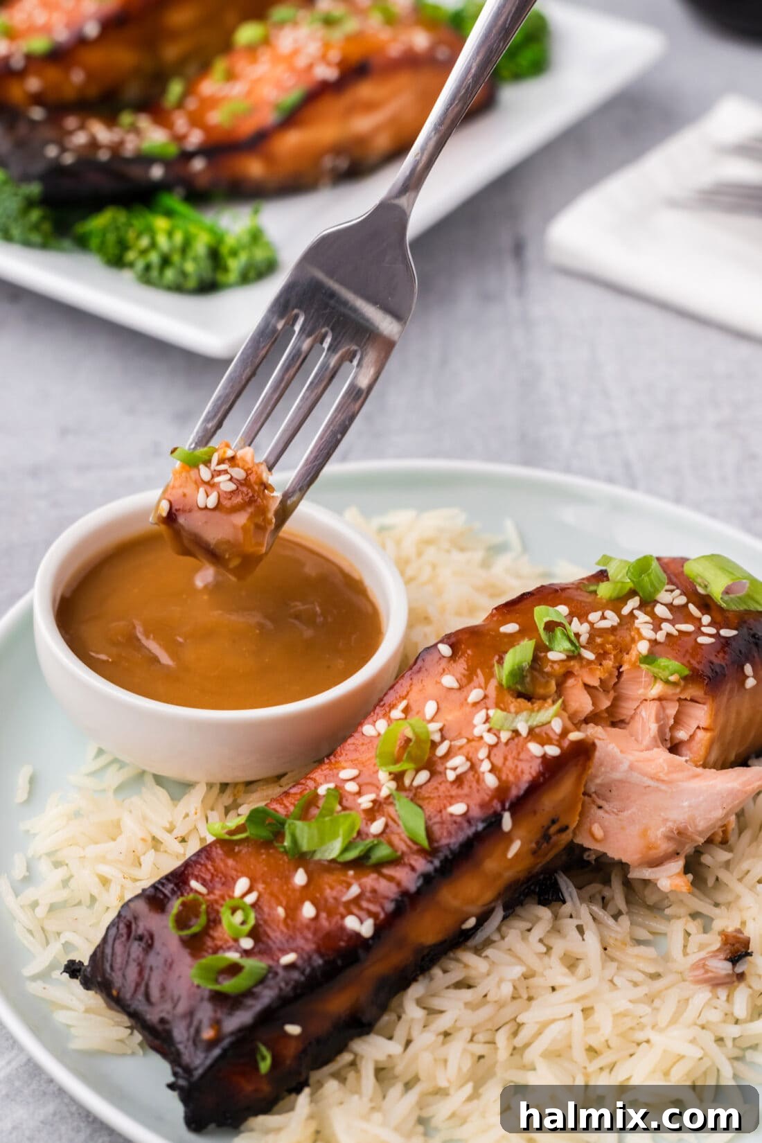 A succulent piece of Miso Salmon being delicately dipped into an extra bowl of rich miso glaze.