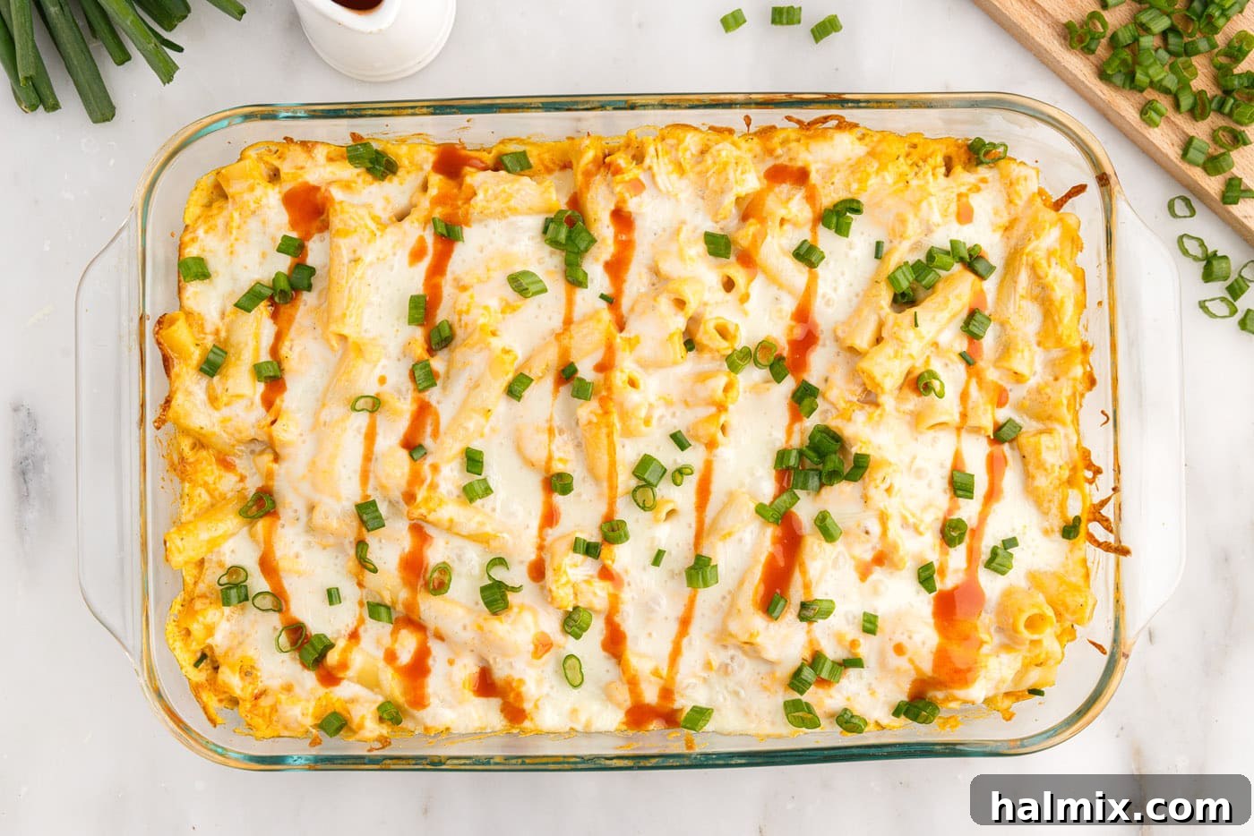 Overhead shot of buffalo chicken casserole garnished with hot sauce and sliced green onions.