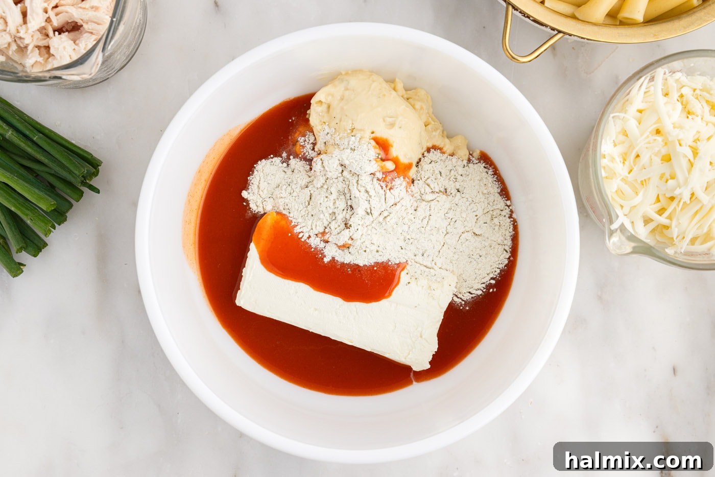 Hot sauce, cream cheese, ranch seasoning mix, and cream of chicken soup in a bowl being mixed together.
