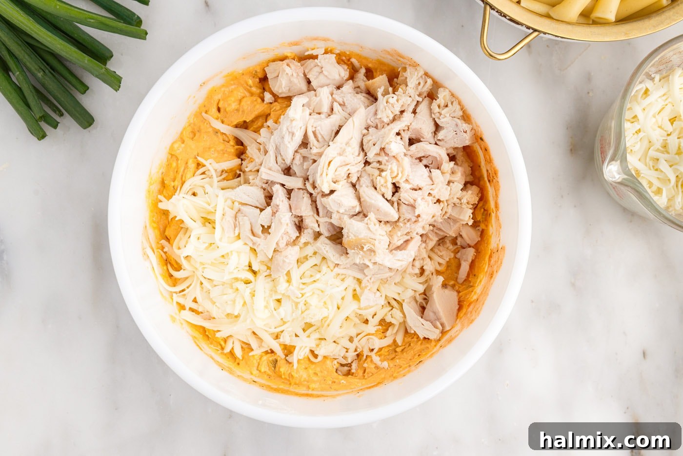 Adding shredded cheese and cooked chicken to the buffalo chicken mixture in a bowl.