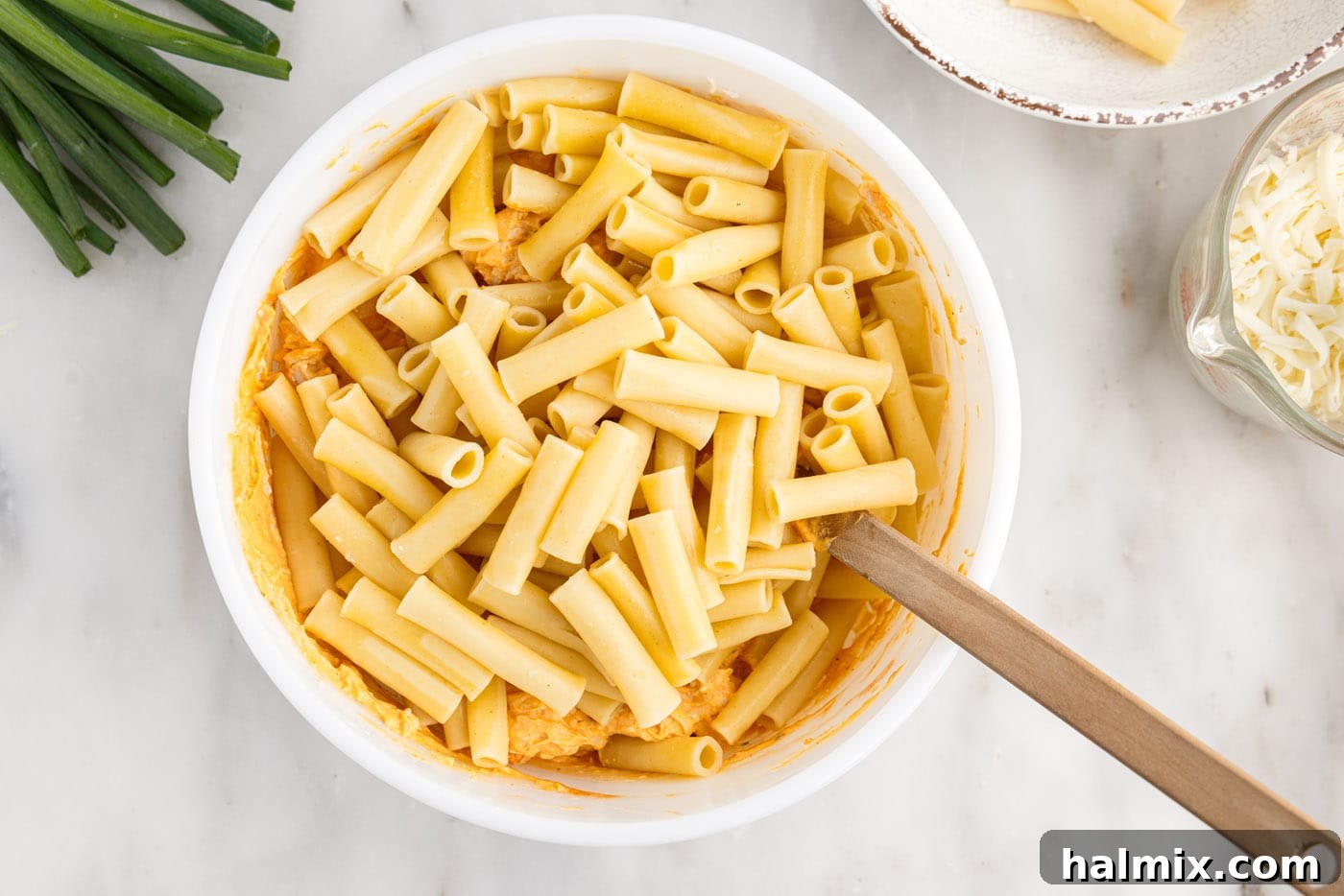 Combining the cooked pasta with the buffalo chicken mixture until everything is evenly coated.