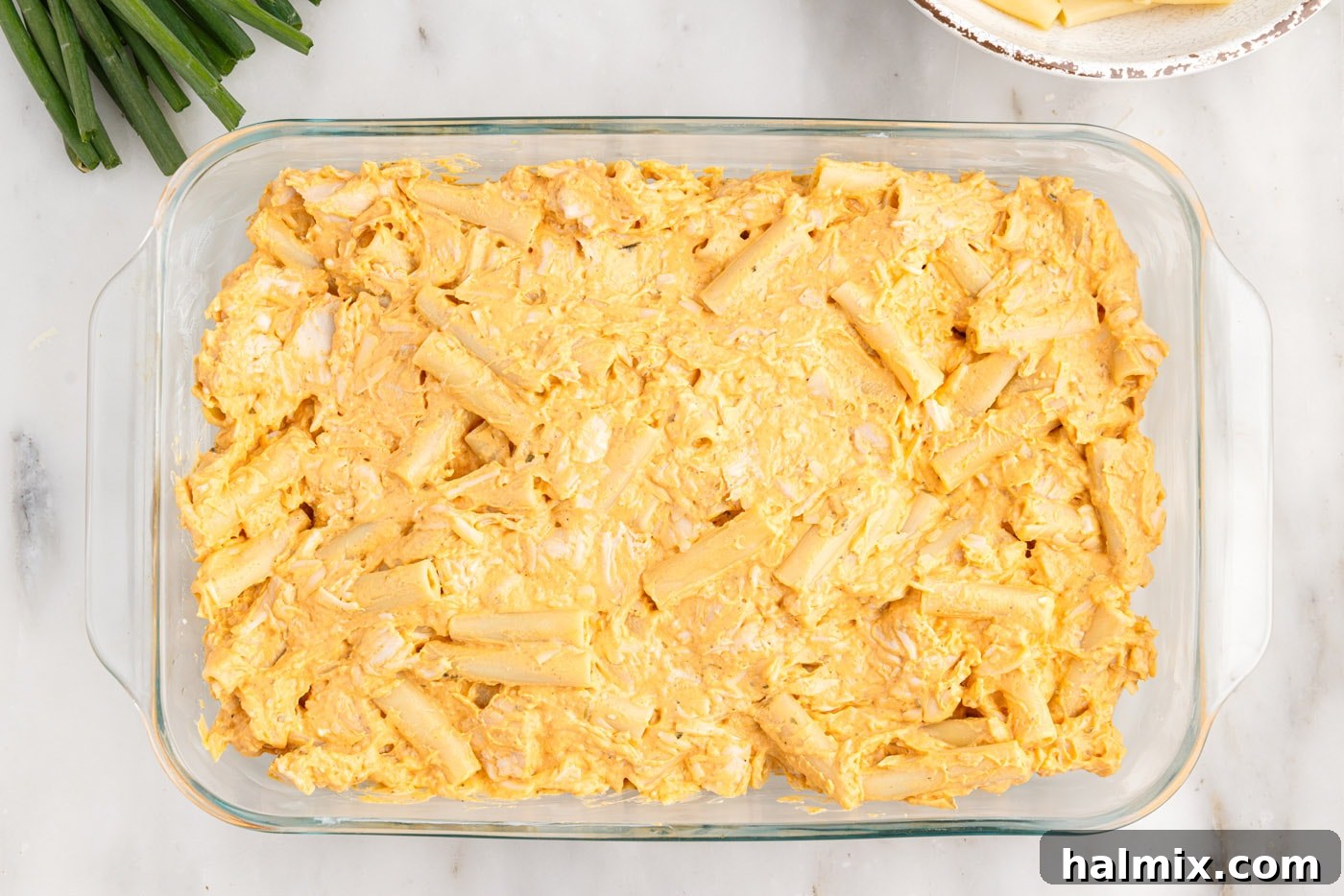 The buffalo chicken pasta casserole mixture spread out in a 9x13 inch baking dish.