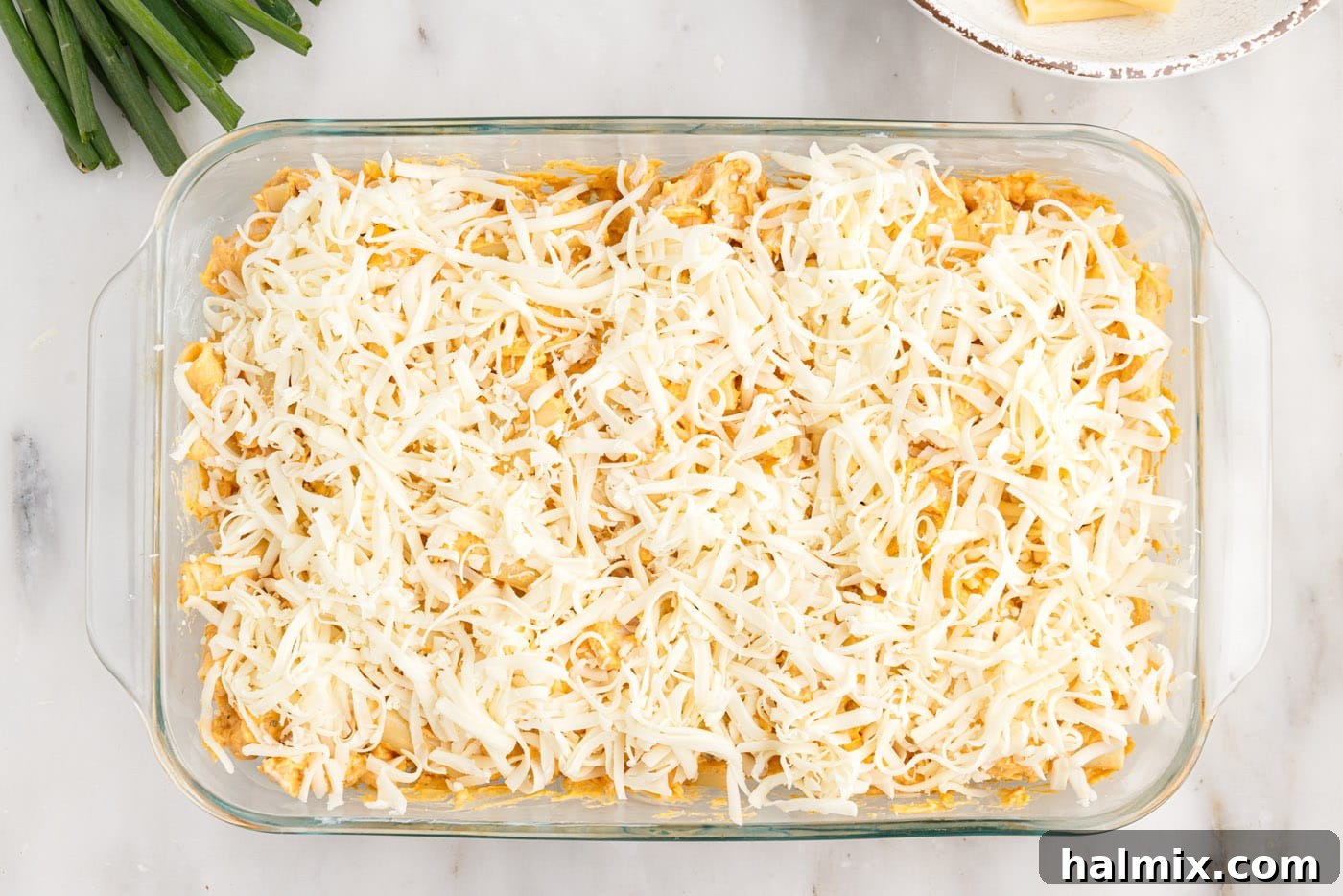 Mozzarella cheese being sprinkled generously on top of the buffalo chicken casserole before baking.