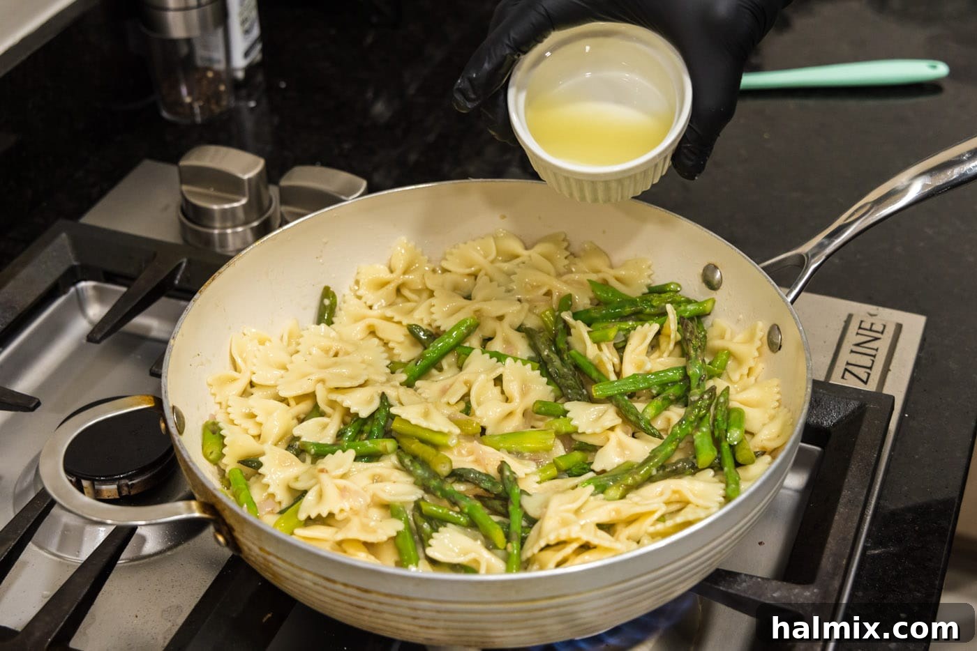 Fresh lemon juice being poured over the asparagus pasta in the skillet, adding a final bright touch.