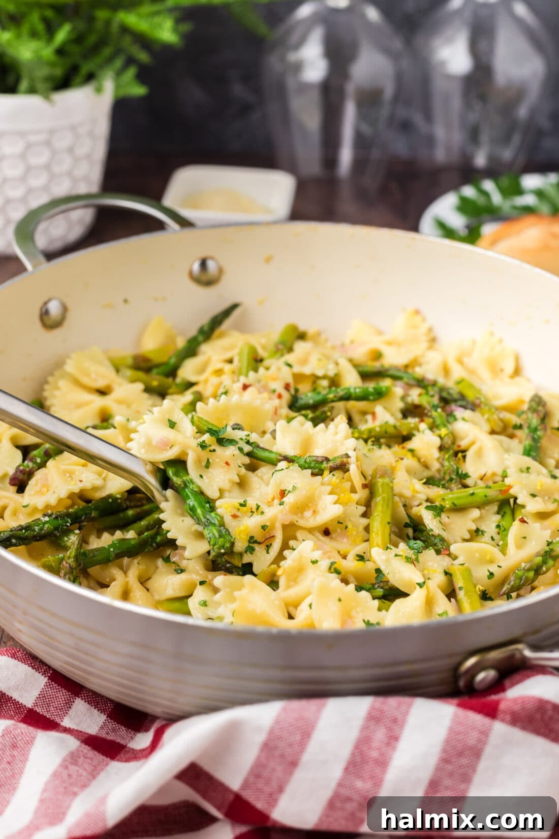 A serving spoon lifting a portion of Asparagus Pasta from a skillet, showing the well-coated pasta and asparagus.