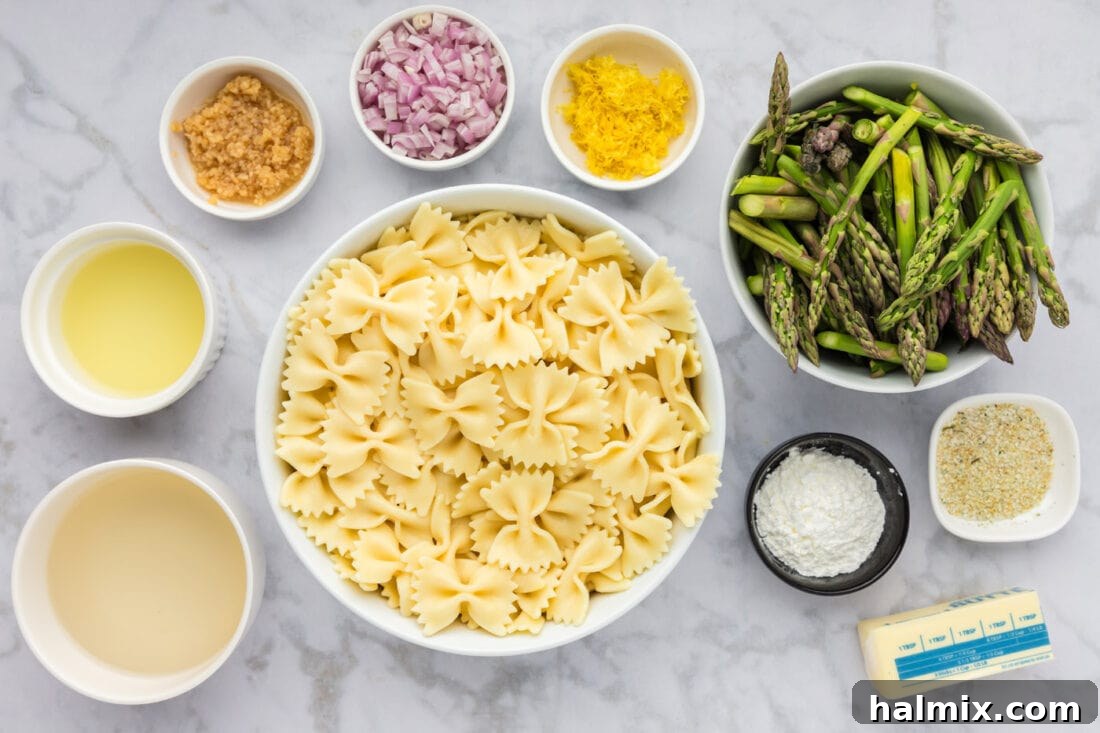A flat lay photograph displaying all the fresh ingredients required for Asparagus Pasta, including asparagus, lemons, butter, garlic, shallots, and dry pasta.