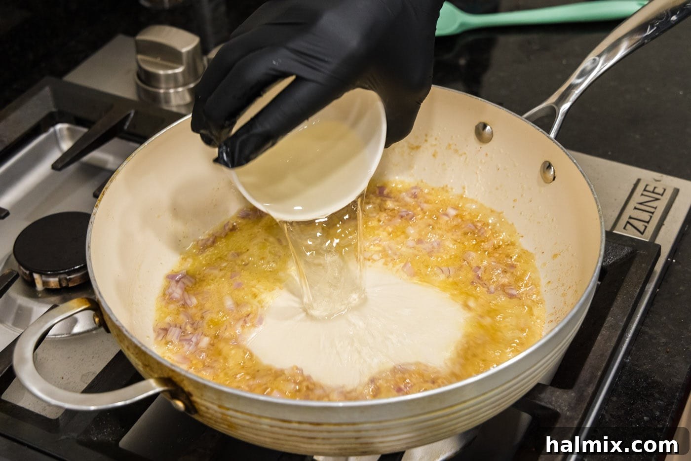 White wine being poured into the skillet with sautéed butter, garlic, and shallots, alongside lemon zest.